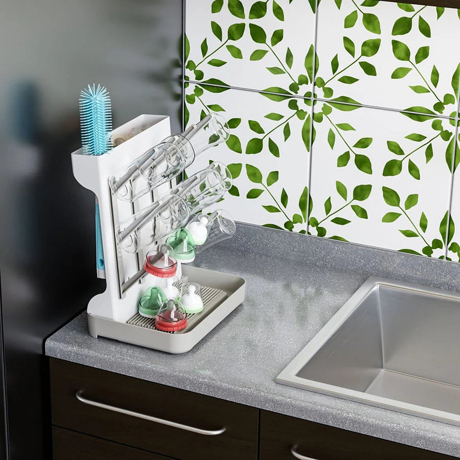 White multi-tier baby bottle drying rack with bottles, nipples, and brush on a kitchen counter.