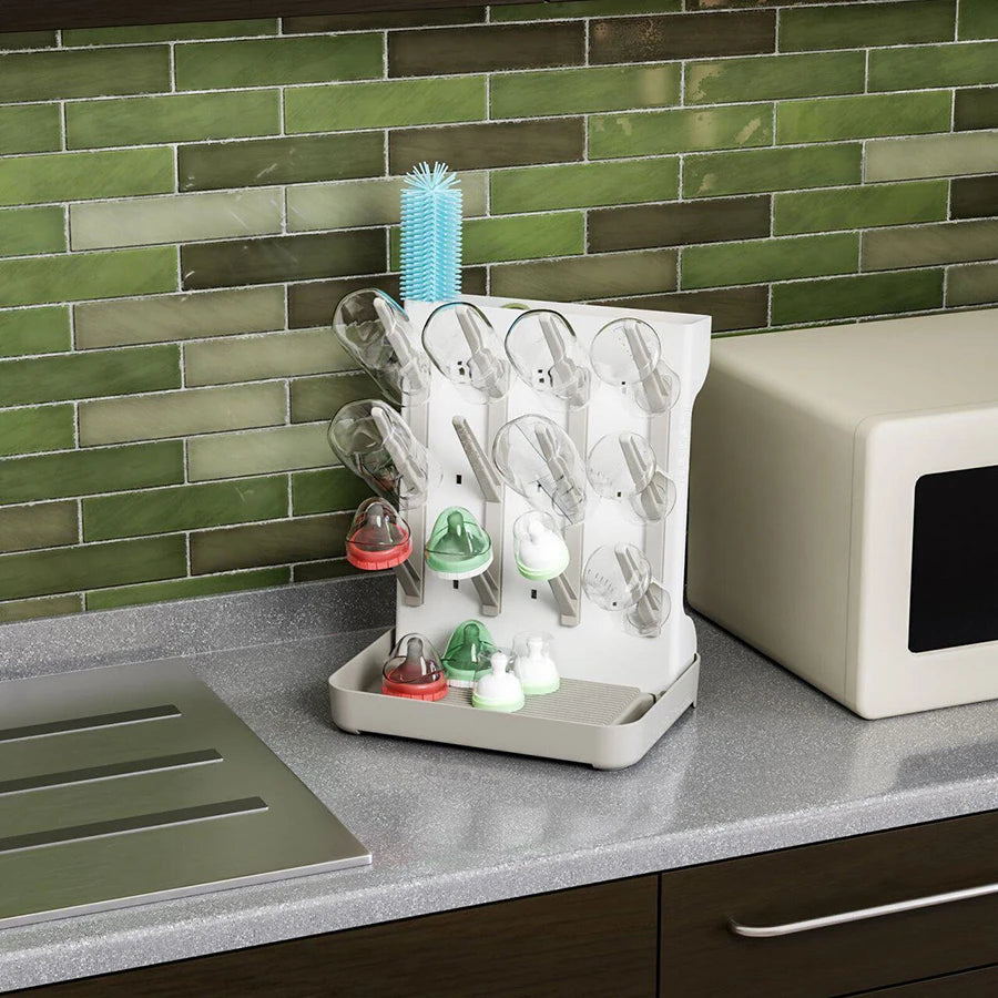 White multi-tier baby bottle drying rack with clear, red, and green bottle parts on a gray counter.