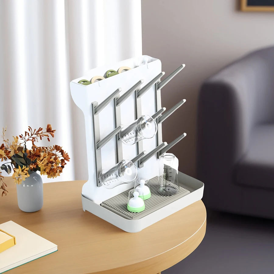 White multi-tier baby bottle drying rack with gray pegs and green accents, holding bottles and cups.