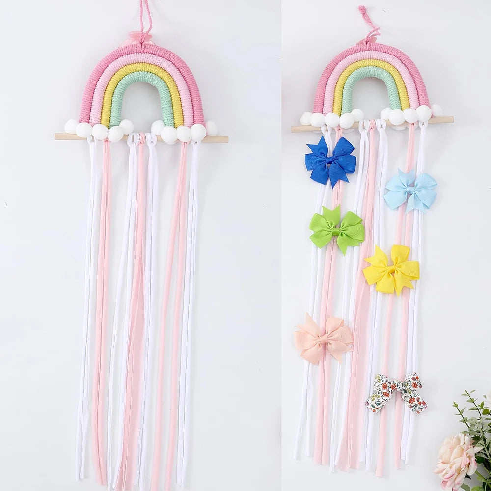 Pink and pastel rainbow wall hanger with white pom-poms and hanging ribbons for hair accessories.
