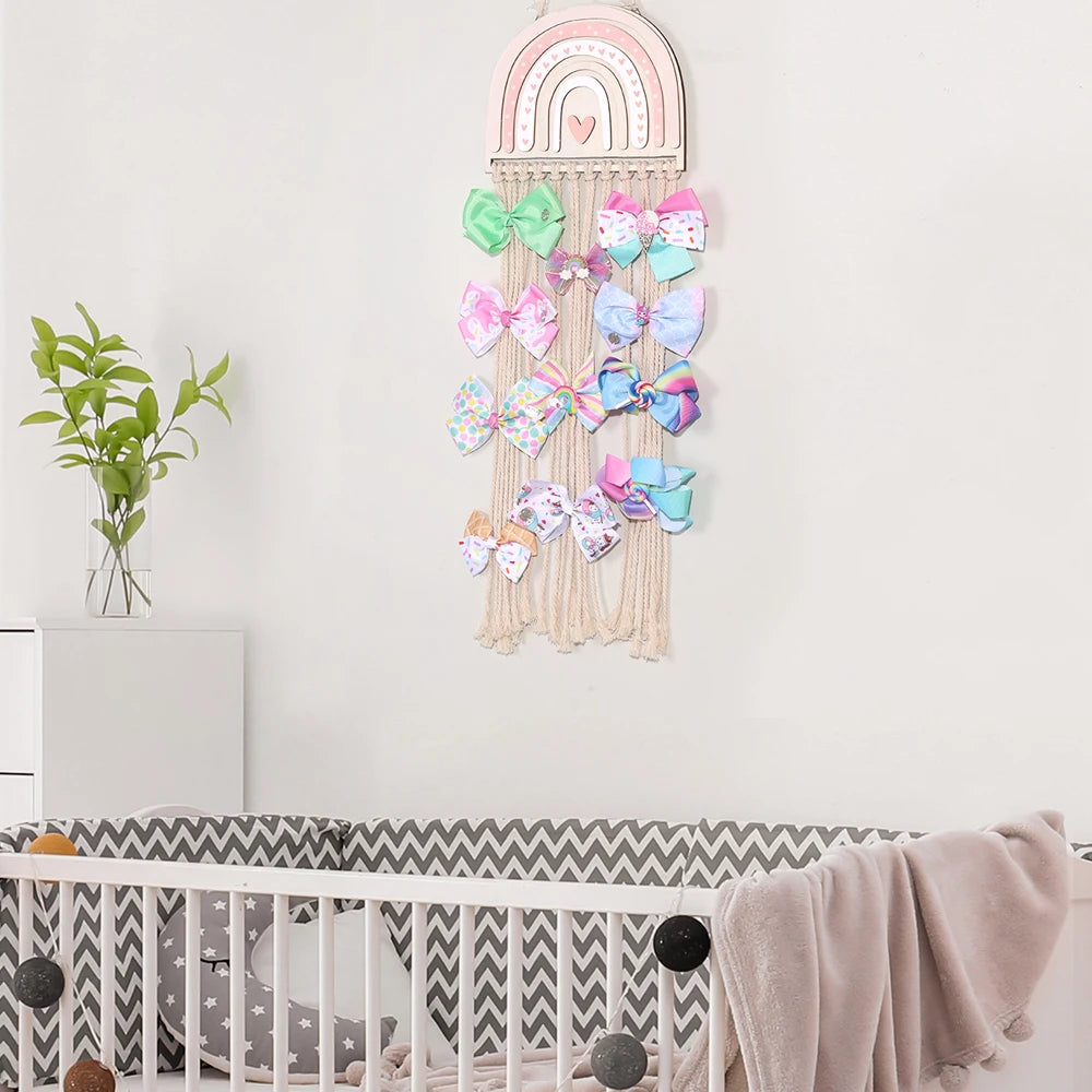 Pink wooden rainbow wall hanger with macrame ropes displaying colorful hair bows above a crib.