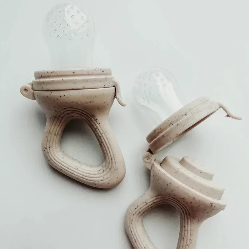 Two speckled beige silicone baby fruit feeders with clear textured nipples, one closed, one open.