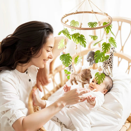 Wooden crib mobile with felt jungle animals and green leaves, hanging over a baby in a crib with a smiling parent.