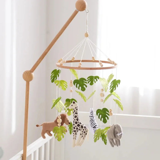 Wooden crib mobile with felt safari animals and green leaves, hanging over a white crib.