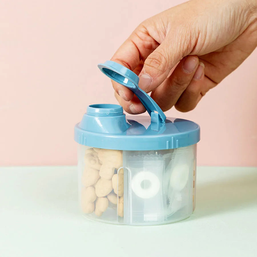 Hand opening a blue and clear 4-compartment portable baby food and formula dispenser with snacks.