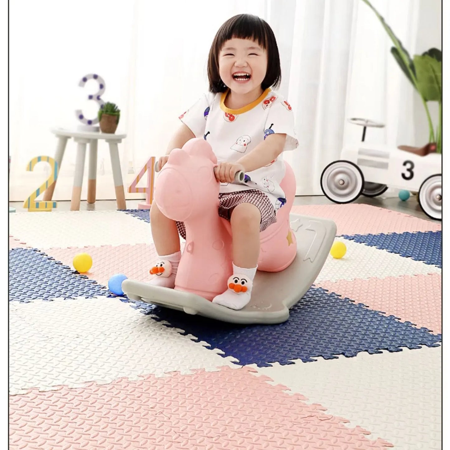 Smiling child on a pink rocking horse on a soft, colorful EVA foam puzzle play mat.