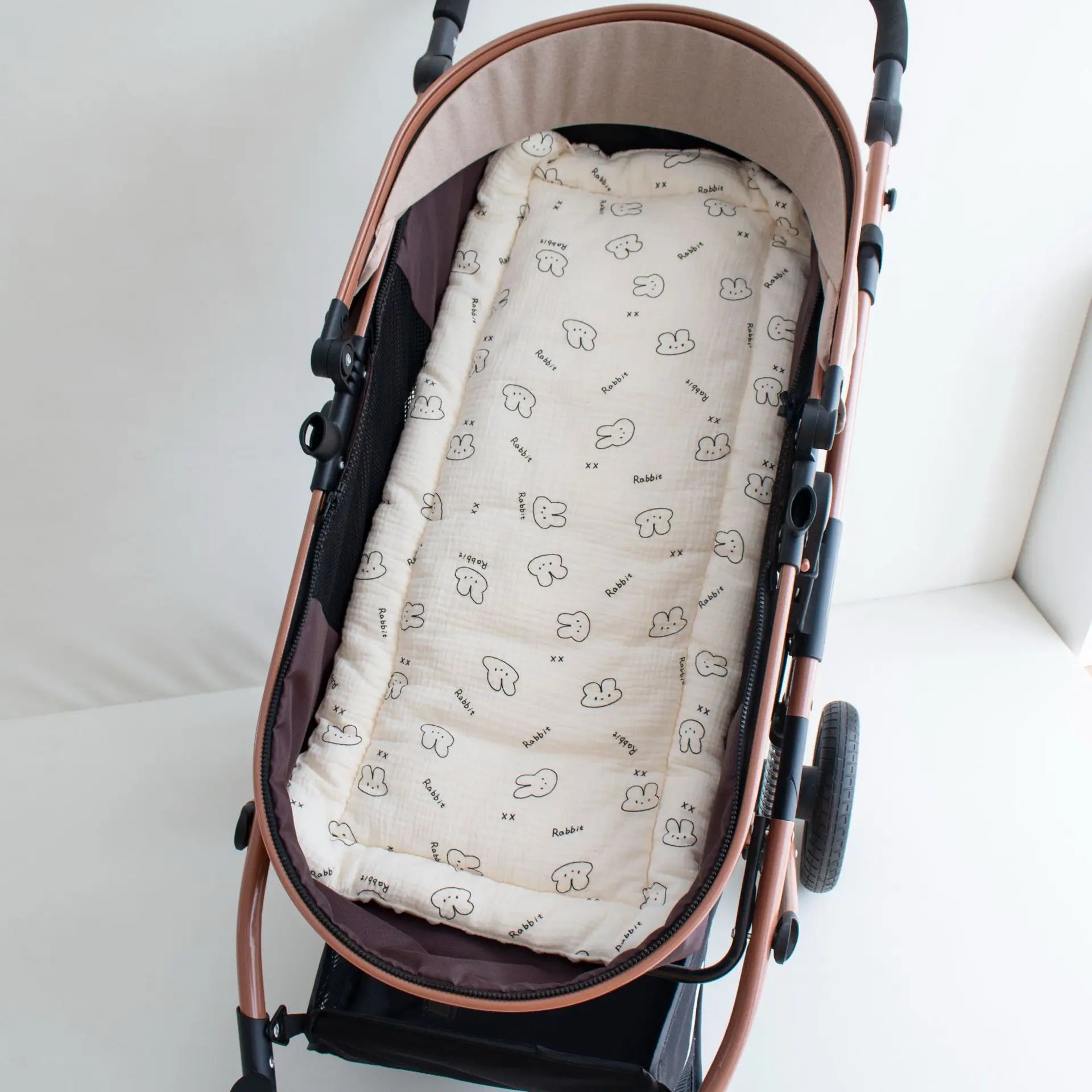 Soft beige cotton stroller cushion with black rabbit print, fitting a rose gold stroller.