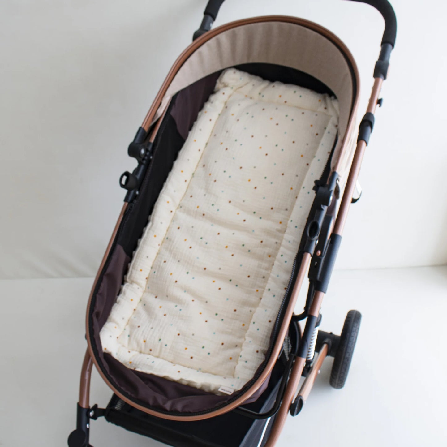 Soft beige stroller cushion with colorful polka dots, nestled in a brown and rose gold stroller.