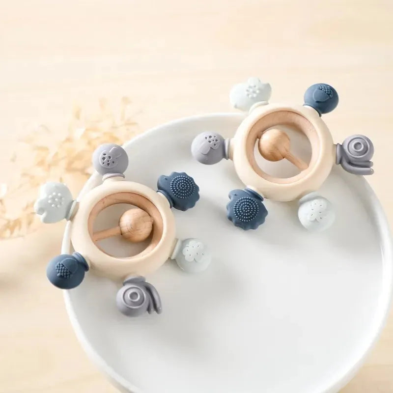 Montessori forest-themed baby silicone and wood teether rattles in muted blue, gray, and cream.