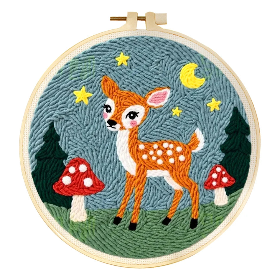 Punch needle embroidery kit featuring a cute fawn, trees, mushrooms, stars, and moon in a wooden hoop.