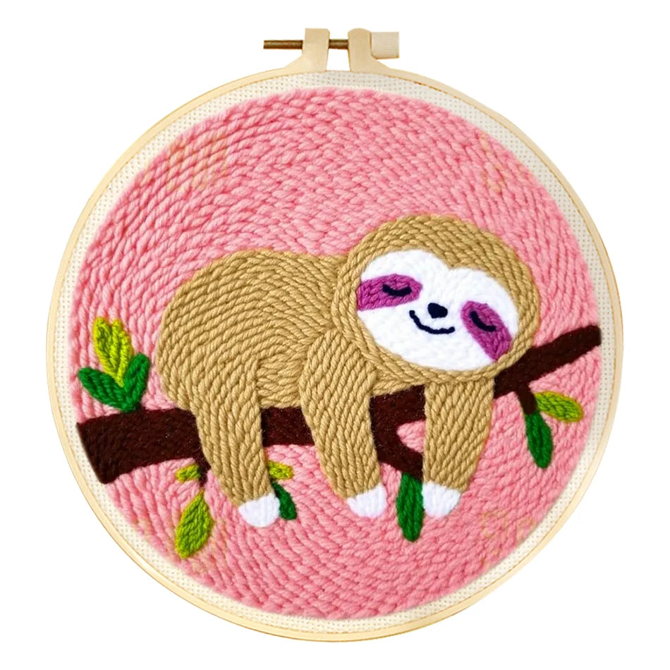 Punch needle embroidery kit featuring a cute brown sloth sleeping on a branch against a pink background in a wooden hoop.