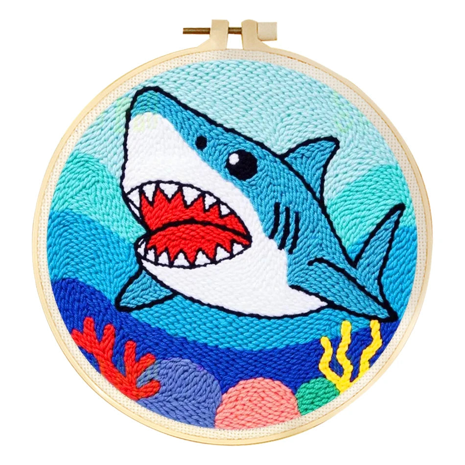 Punch needle embroidery kit featuring a blue shark, coral, and waves in a wooden hoop.