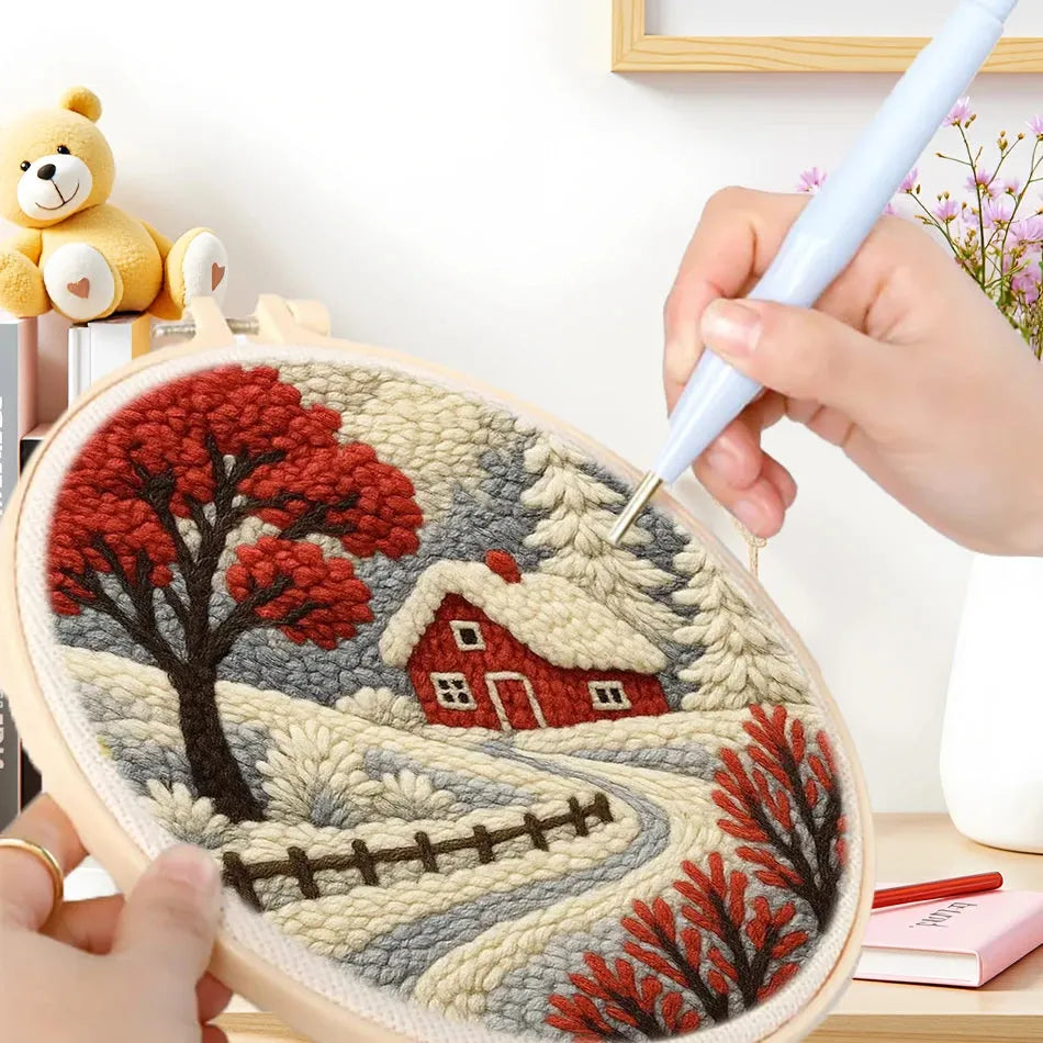 Punch needle kit creating a winter landscape with a red house, snowy trees, and a path in an oval hoop.
