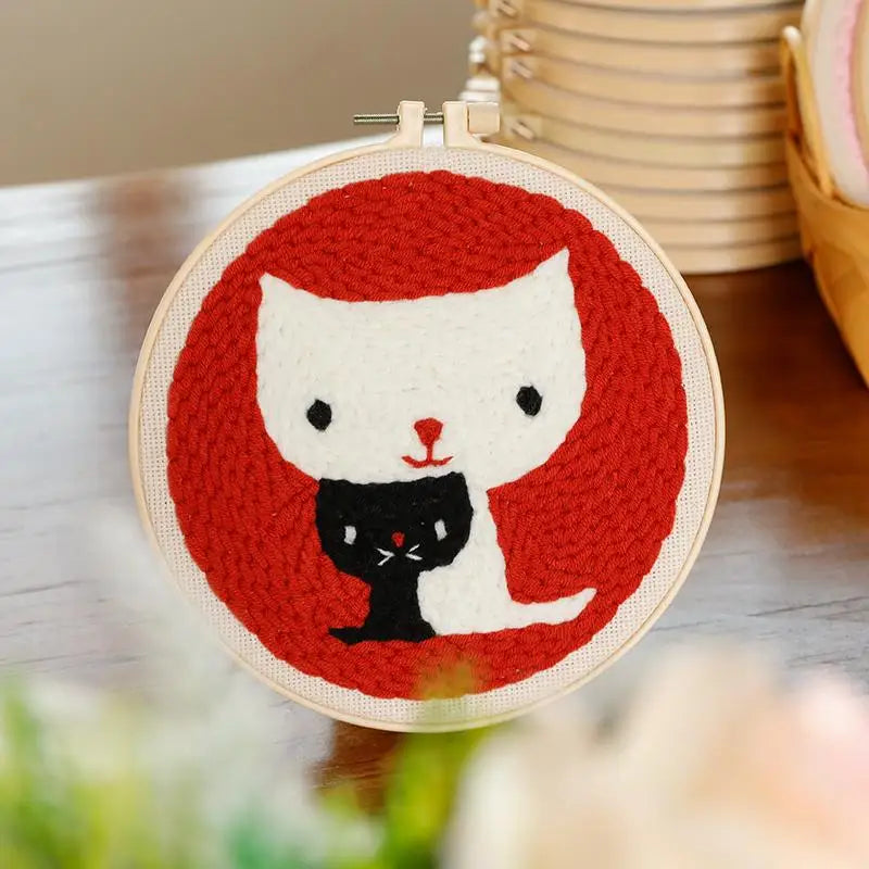 Punch needle embroidery kit featuring a white cat hugging a black cat on a red background, in a wooden hoop.