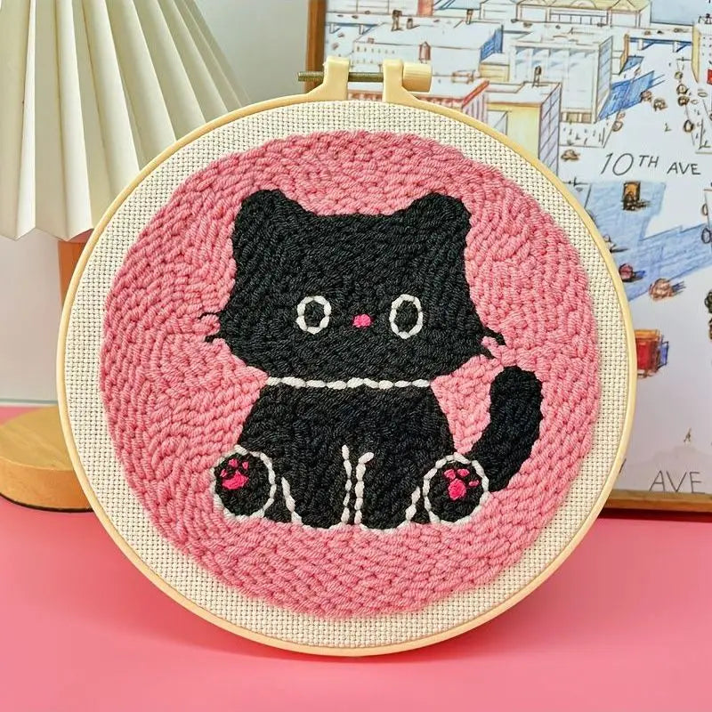 Punch needle embroidery kit featuring a cute black cat on a pink background, framed in a wooden hoop.