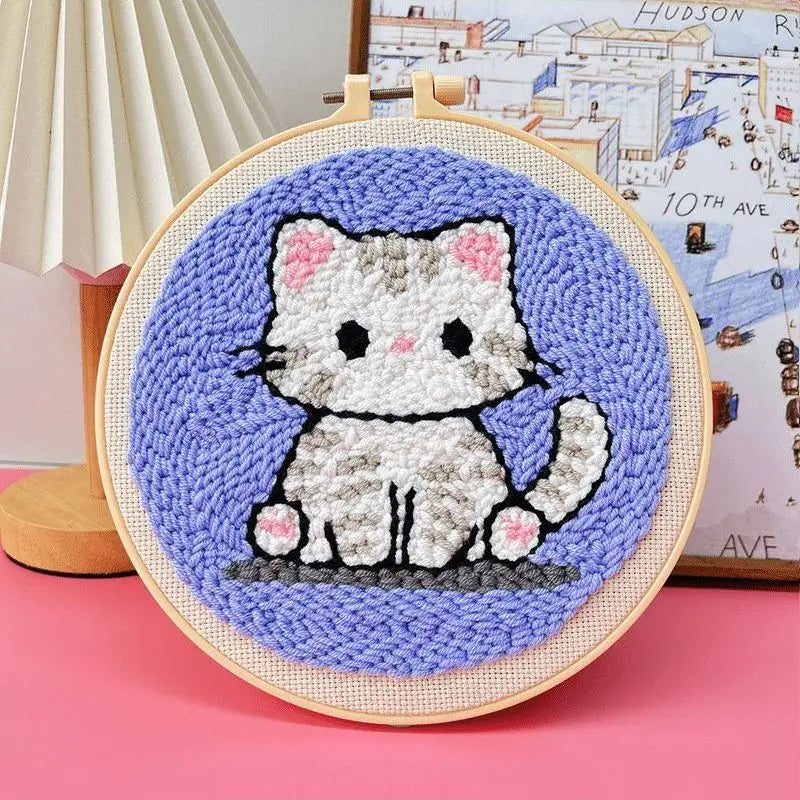 Punch needle embroidery kit featuring a cute gray and white cat on a purple background, framed in a wooden hoop.