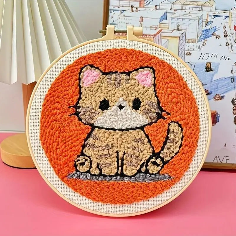 Punch needle embroidery kit featuring a cute brown and black cat on an orange background, framed in a wooden hoop.