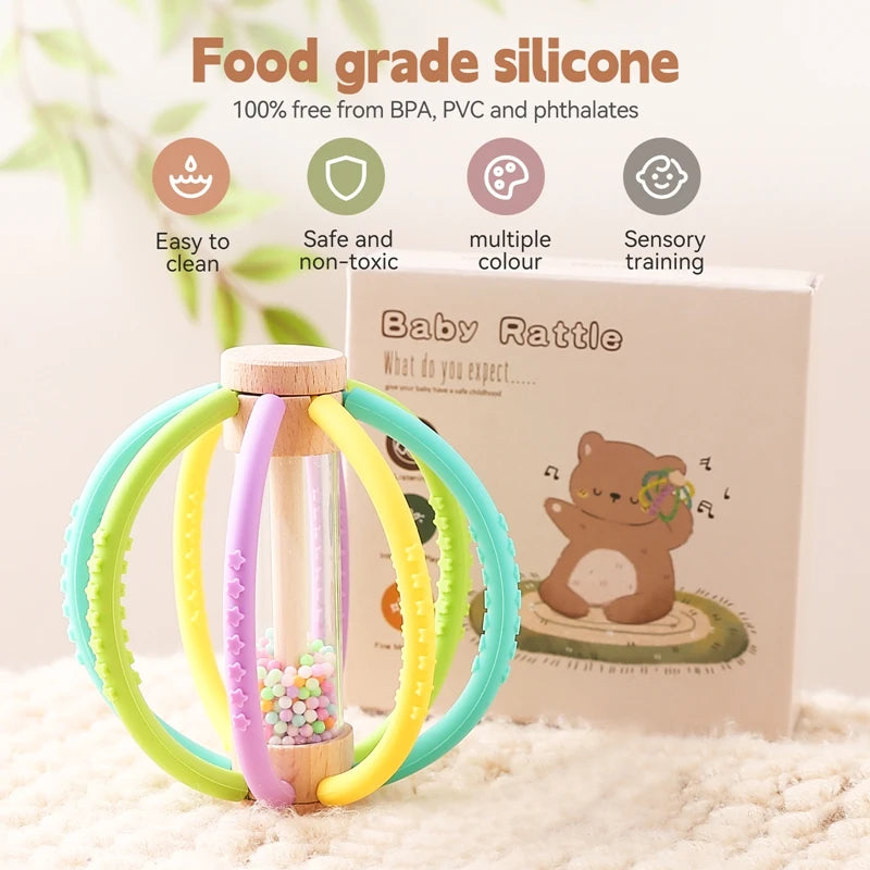 Wooden baby rattle with colorful silicone rings, rain drum, and teether, next to its packaging.