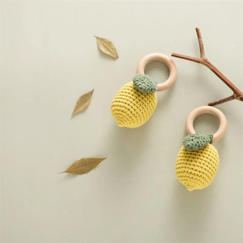 Two yellow crocheted fruit rattles with green leaves and natural wooden rings.