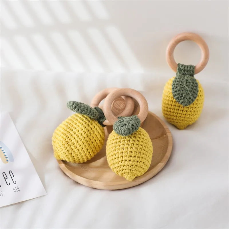 Three yellow crocheted lemon rattles with green leaves and natural wooden rings.