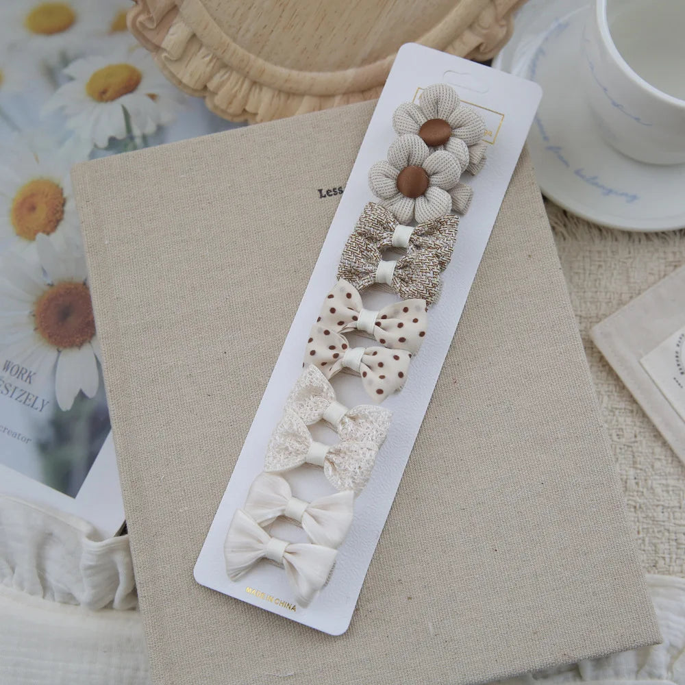 Set of 10 beige and cream fabric hair clips for babies and girls, featuring bows and flower designs.