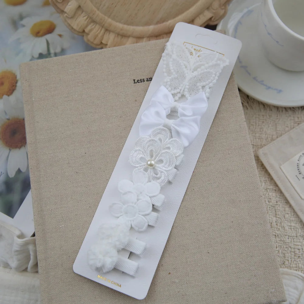 Set of 5 white fabric hair clips for babies and girls, featuring bows, flowers, and a butterfly design.