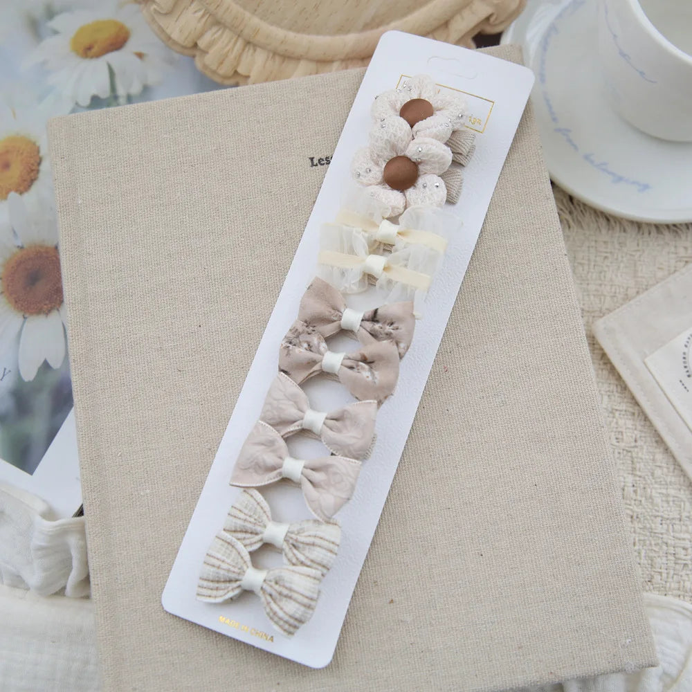 Set of 10 beige and white cotton bow and flower hair clips for babies and girls.
