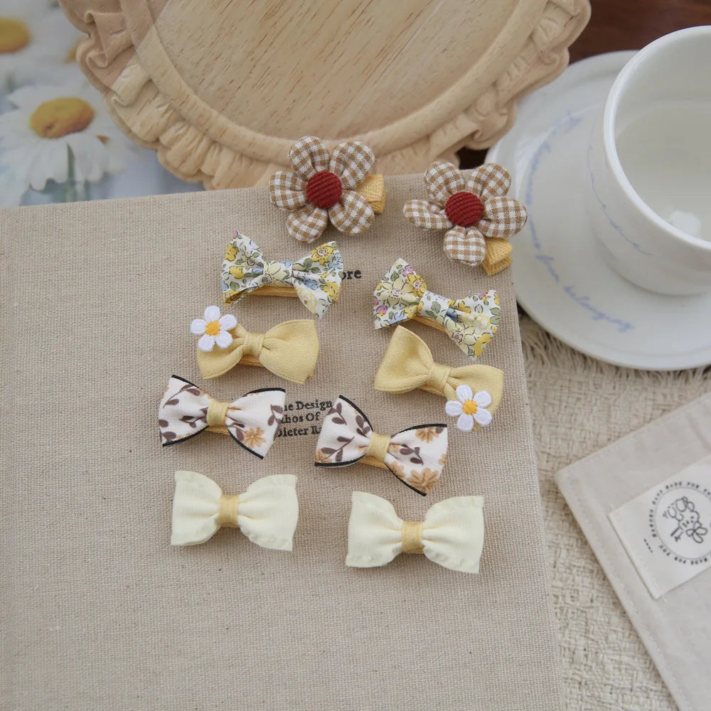 Set of 10 baby girls' hair clips with soft fabric bows in yellow, floral, and gingham patterns.