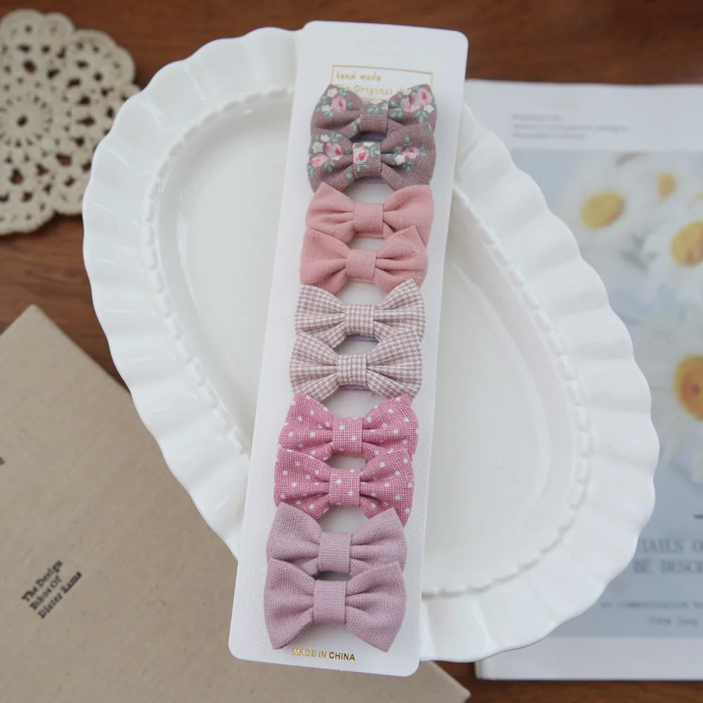 Set of 6 pink and floral fabric bow hair clips for babies and girls, on a white plate.