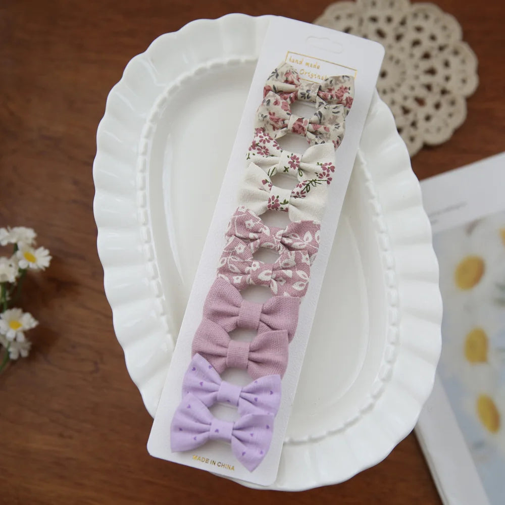 Set of 10 fabric bow hair clips for babies and girls in floral and solid pastel designs.