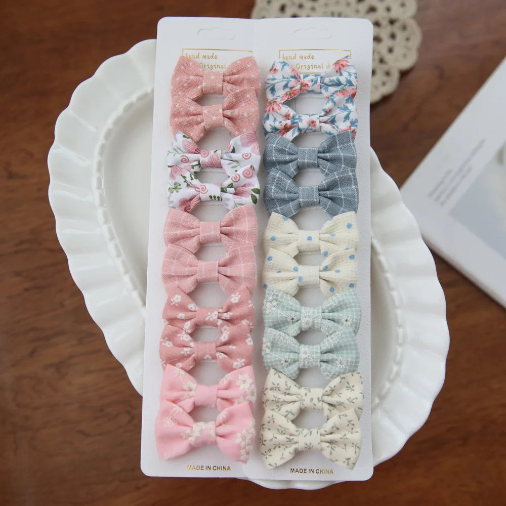 Set of 10 baby girl hair clips with fabric bows in pink, blue, and floral patterns.