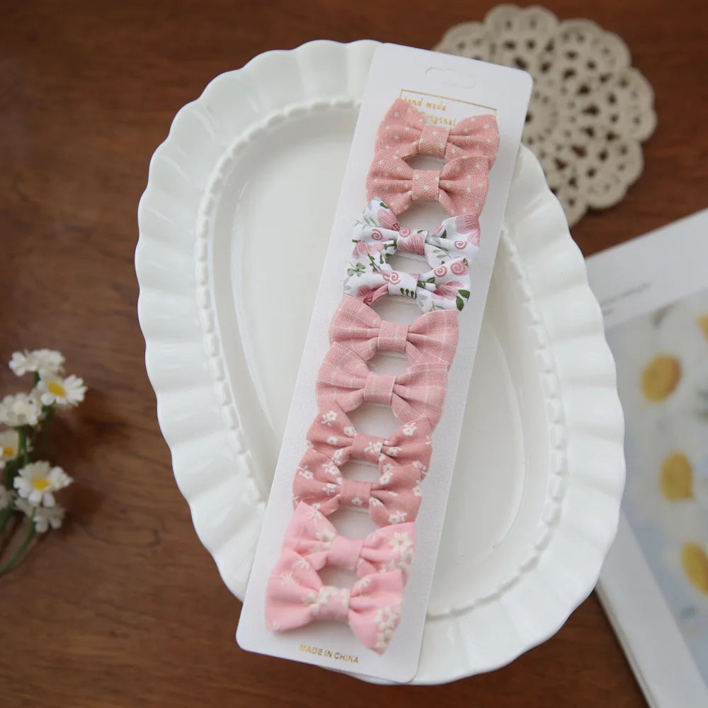 Set of 10 pink and floral fabric bow hair clips for babies and girls, on a white display card.