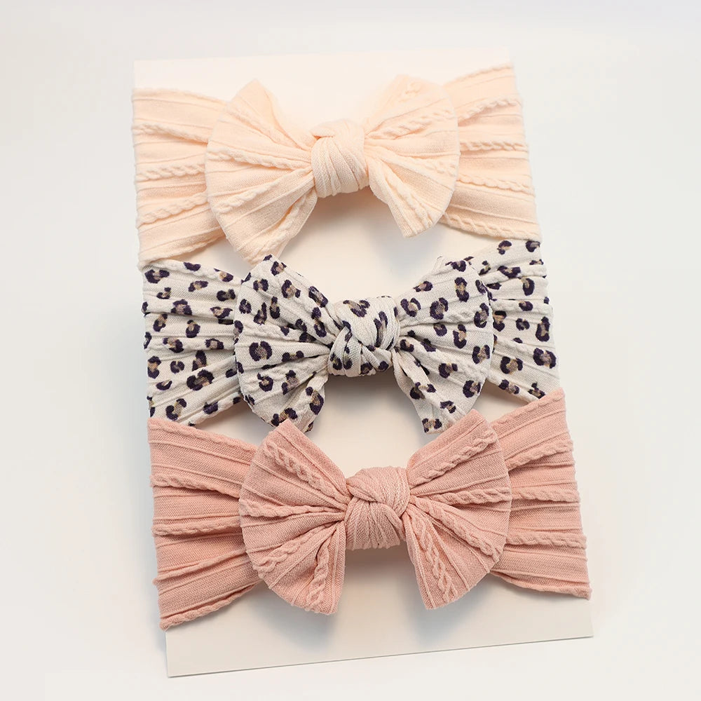 Set of 3 soft nylon baby headbands: peach ribbed, leopard print, and pink ribbed bows.