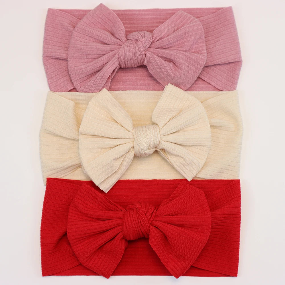 Set of 3 soft, flexible nylon baby headbands with bows in pink, cream, and red.