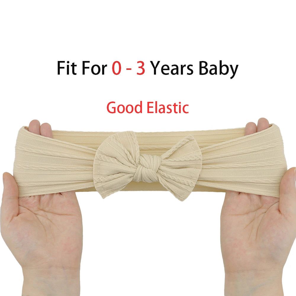 Hands holding a soft, flexible beige nylon baby headband with a textured bow, suitable for ages 0-3.