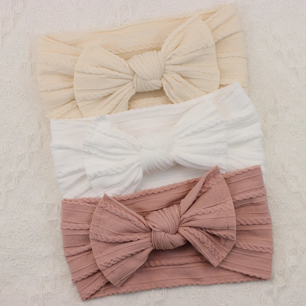 Set of 3 soft nylon baby headbands with bows in cream, white, and dusty rose.