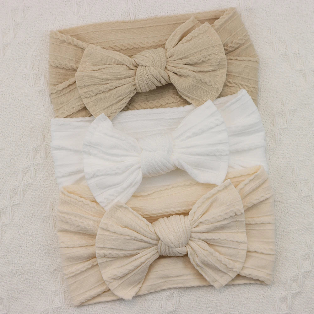 Set of 3 soft nylon baby headbands with bows in beige, white, and light cream.