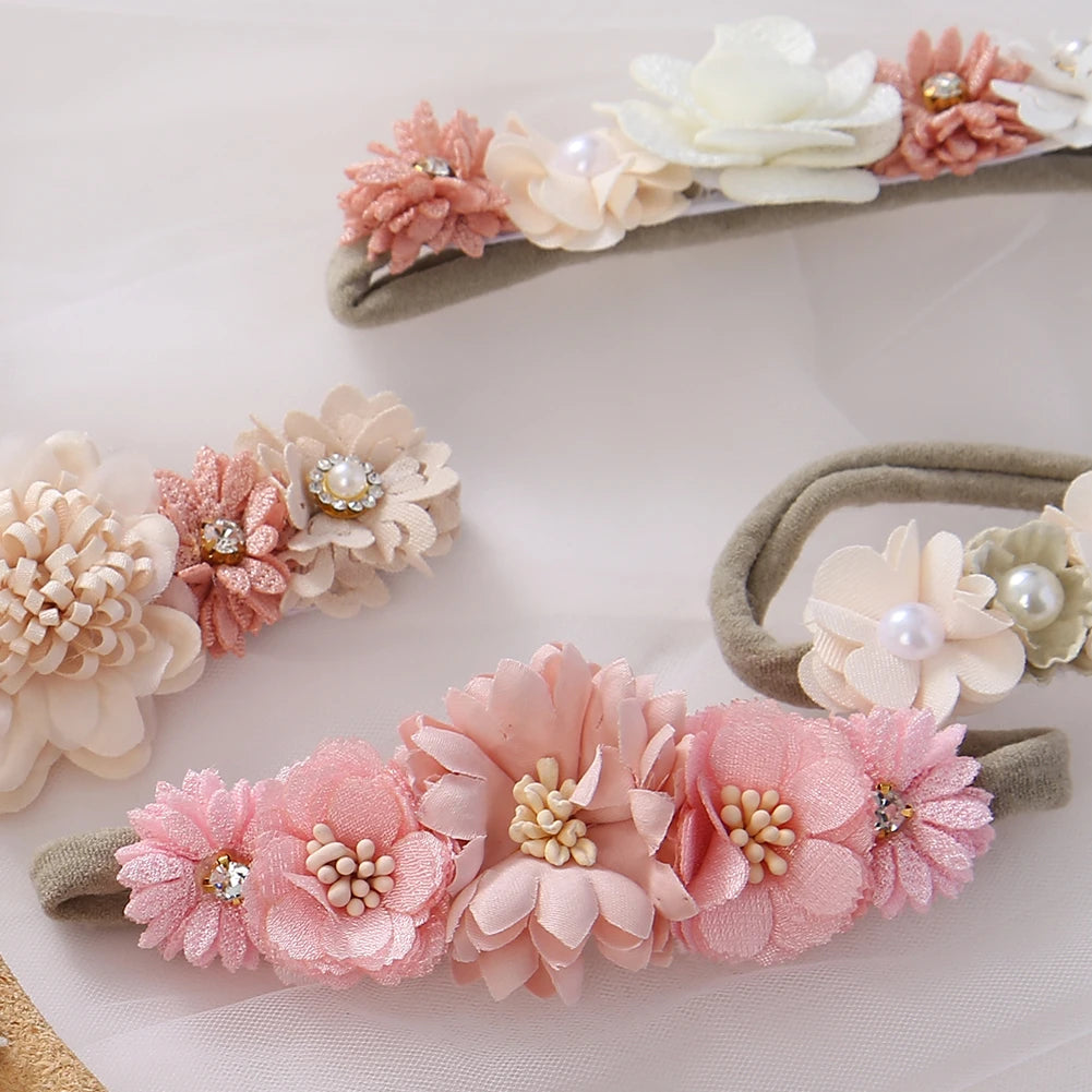 Set of 3 soft nylon baby headbands with assorted pink and cream floral designs, pearls, and rhinestones.