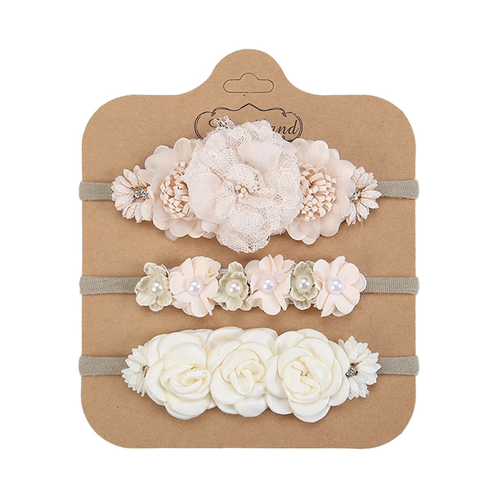 Set of 3 soft nylon baby headbands with delicate floral designs in cream, pink, and white.