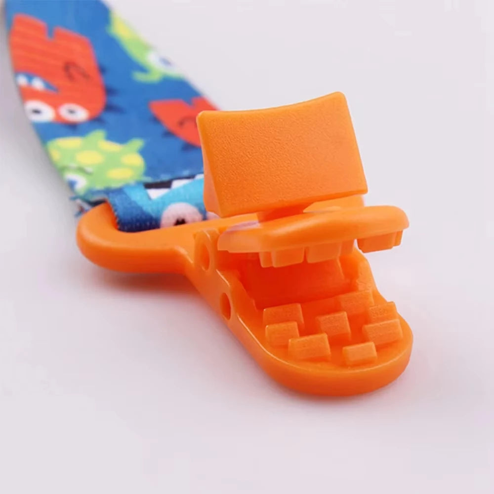 Blue polyester pacifier clip with colorful monster print and an orange plastic clasp.