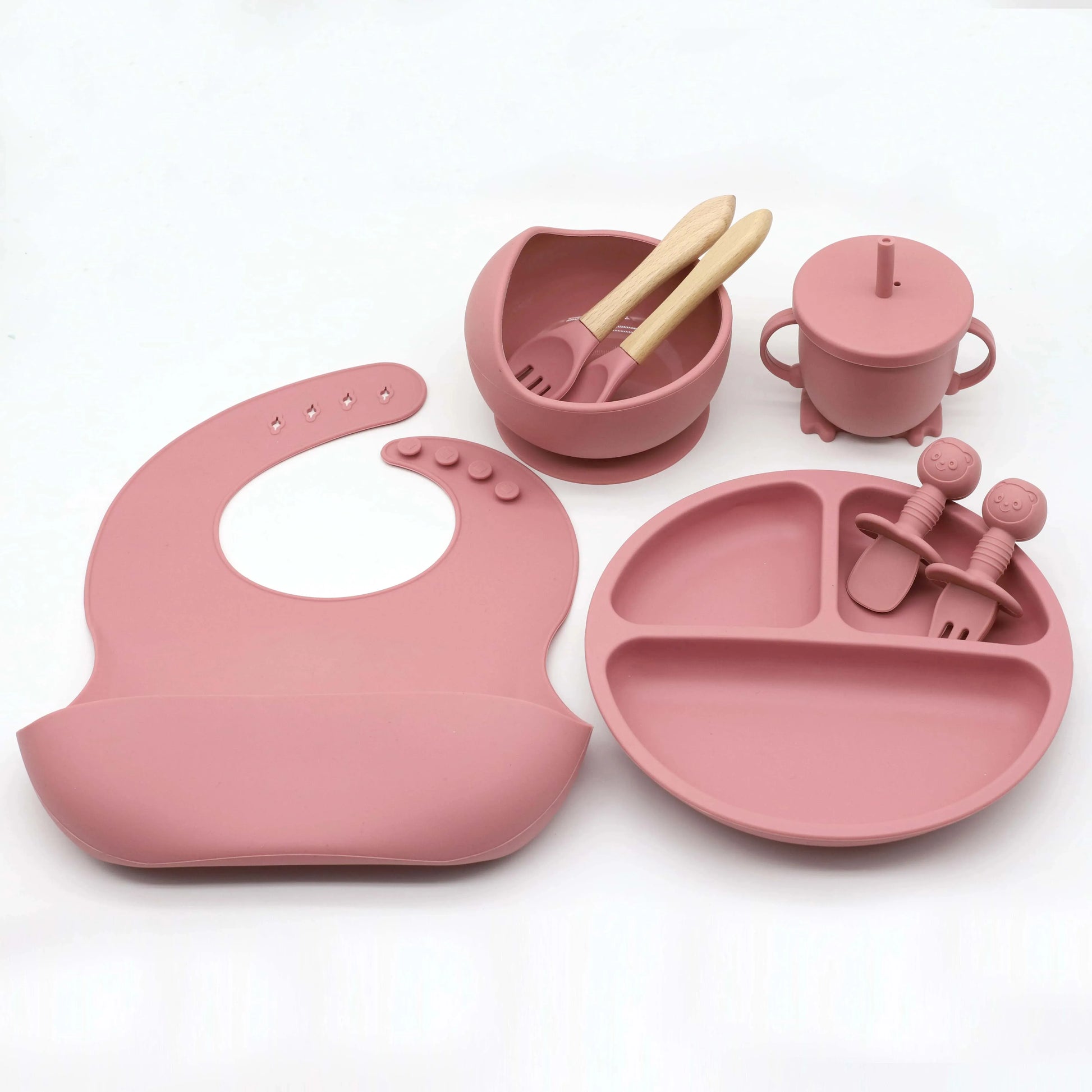 Pink silicone 8-piece baby feeding set with bib, suction plate, bowl, cup, and utensils.
