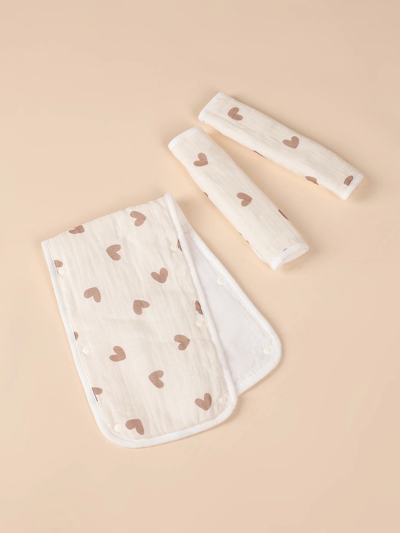 Soft beige stroller handle cover and two safety belt pads with brown heart patterns.