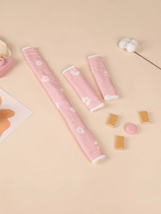 Pink daisy-print stroller handle cover and two matching safety belt pads on a beige surface.