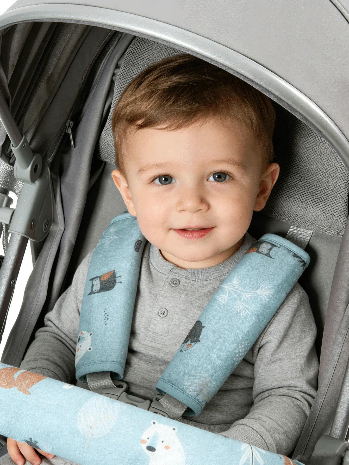 Baby in a gray stroller with blue, patterned safety harness pads and a matching handle cover.