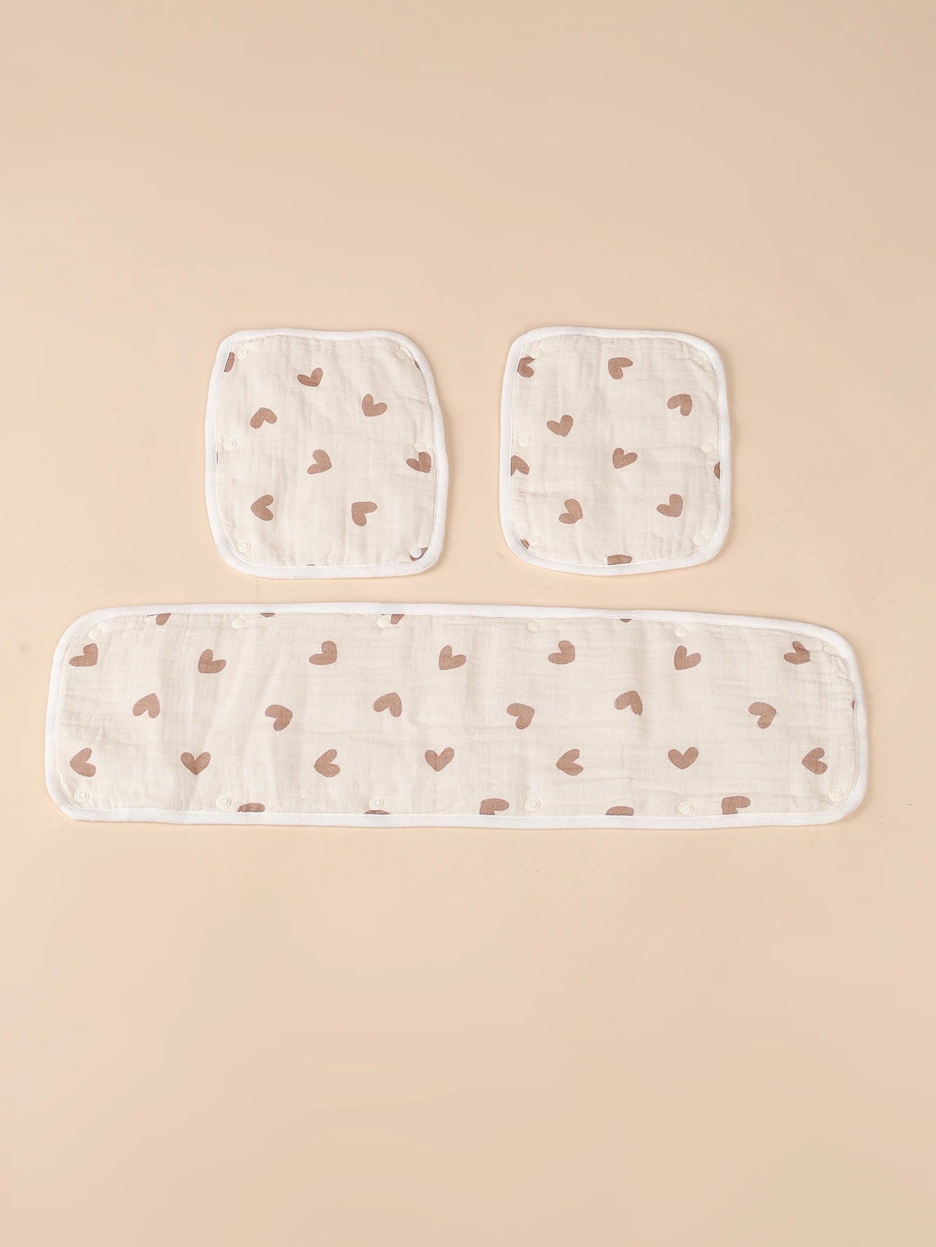 Beige baby stroller handle cover and two seat belt pads with brown heart print.