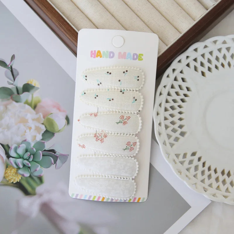 Set of 6 handmade white cotton snap hair clips for girls, featuring delicate floral and cherry patterns.