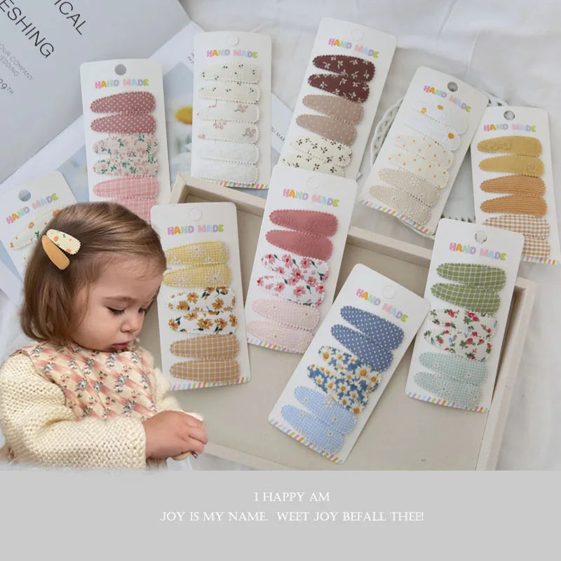 Assortment of 6 handmade floral and patterned fabric snap hair clips for girls, with a toddler wearing one.