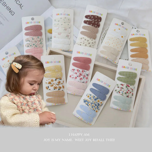 Assortment of 6 handmade floral and patterned fabric snap hair clips for girls, with a toddler wearing one.