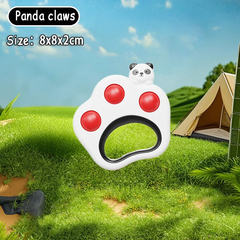 White panda paw fidget toy with red pop-it buttons, 8x8x2cm, on grass with a tent.