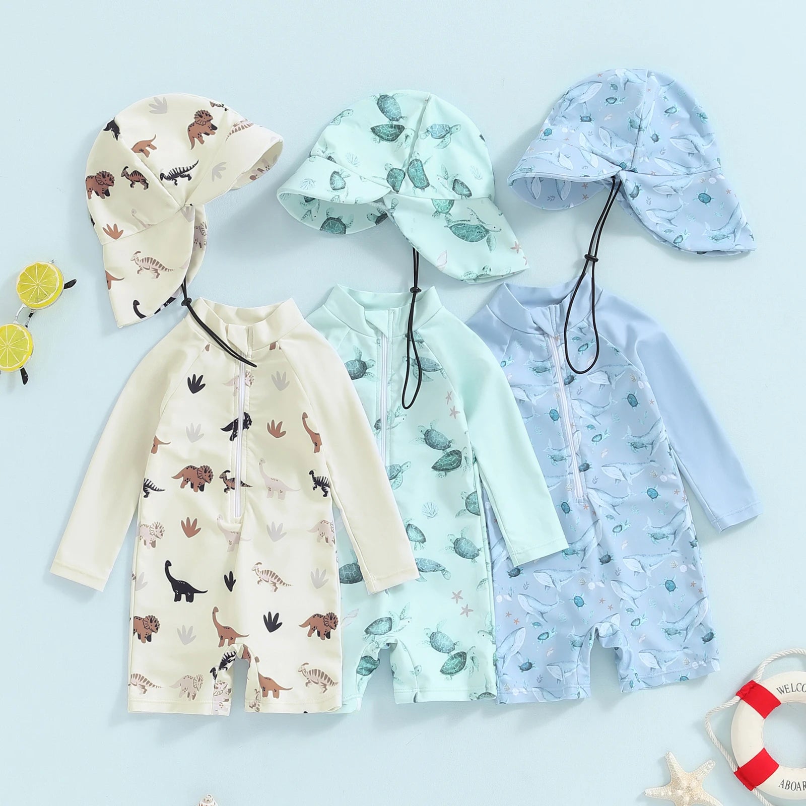 Three long-sleeve baby swimsuits with sun hats: dinosaur print, green turtle, and blue whale designs.